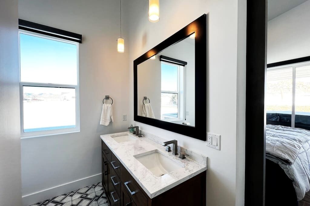 A modern bathroom with a large mirror, two sinks, and a window.