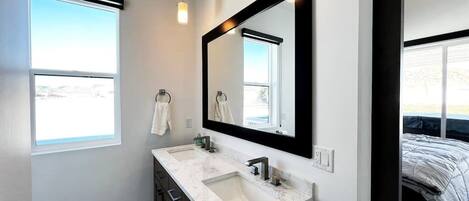 A modern bathroom with a large mirror, two sinks, and a window.