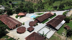 An aerial view of a resort with multiple buildings, a swimming pool, and surrounding greenery. - CONDOMÍNIO FAZENDA TRÊS TESOUROS (Bonito)