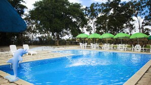 A swimming pool with white lounge chairs and green umbrellas, surrounded by trees. - CONDOMÍNIO FAZENDA TRÊS TESOUROS (Bonito)