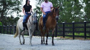 Two people riding horses on a gravel path with a wooden fence in the background. - CONDOMÍNIO FAZENDA TRÊS TESOUROS (Bonito)
