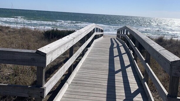 En träpromenad som leder ner till havet, med en klar himmel.