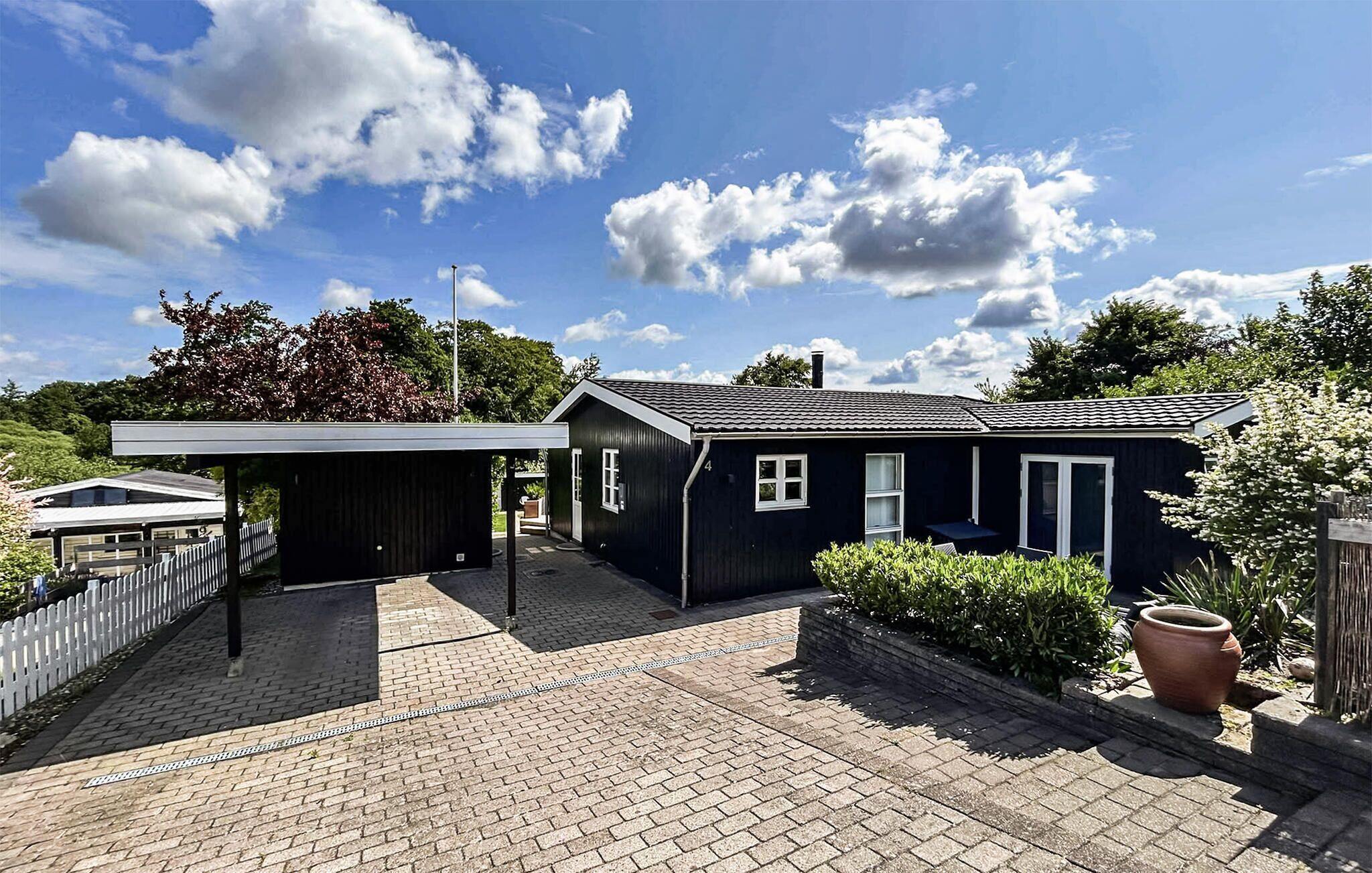 Ett modernt svart hus med en inglasad veranda och en uppfart belagd med tegelstenar.