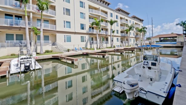 Un puerto deportivo con barcos amarrados, un edificio con balcones y palmeras.