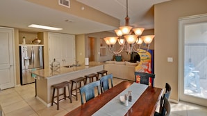 Una cocina amplia con una isla central, un comedor con una mesa larga y un candelabro luminoso.