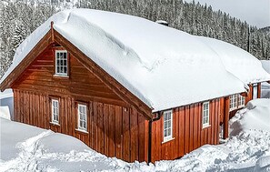 Eine Holzhütte mit schneebedecktem Dach, umgeben von Schnee und Bäumen.