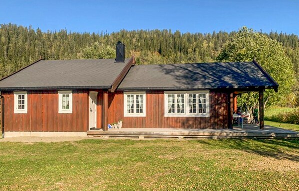Ein eingeschossiges Holzhaus mit dunklem Dach, einer Veranda und einem gepflegten Rasen.