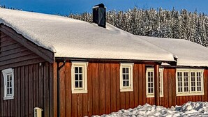 Une cabane en bois, dont le toit est recouvert de neige, avec une forêt en arrière-plan.