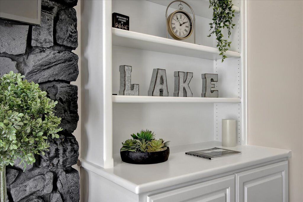 Een witte inbouwplank met de tekst “LAKE” in grote letters, een klok en een kleine plant in een pot.