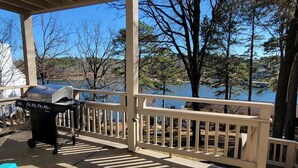 A covered outdoor area with a grill, a blue chair, and a view of a lake and trees.