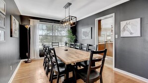 A dining area with a wooden table and chairs, a hanging light fixture, and framed artwork on the walls.