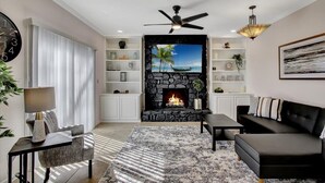 A modern living room with a fireplace, a ceiling fan, and a large TV screen.