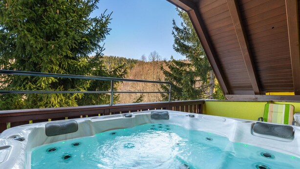 A hot tub with a wooden deck and metal railing, surrounded by trees and a clear sky. - Nice home in Lokve with sauna (Lokve)