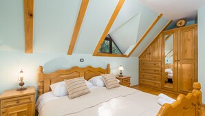 A bedroom with a sloped ceiling, wooden headboard, two bedside tables with lamps, a large mirror, and a wardrobe. - Nice home in Lokve with sauna (Lokve)