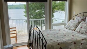 A bedroom with a bed, a ceiling fan, and a view of a lake through large windows. - Water and Beach Front Property 4 season on Ottawa River with Private Boat Launch (Deep River)
