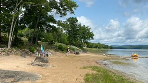 A sandy beach with a rocky outcrop, a small boat, and a person walking. - Water and Beach Front Property 4 season on Ottawa River with Private Boat Launch (Deep River)