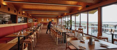 Un restaurante espacioso con interiores de madera, ventanas amplias y vistas al agua.