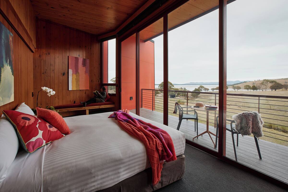 A bedroom with a large bed, a view of the outdoors, and a wooden ceiling.