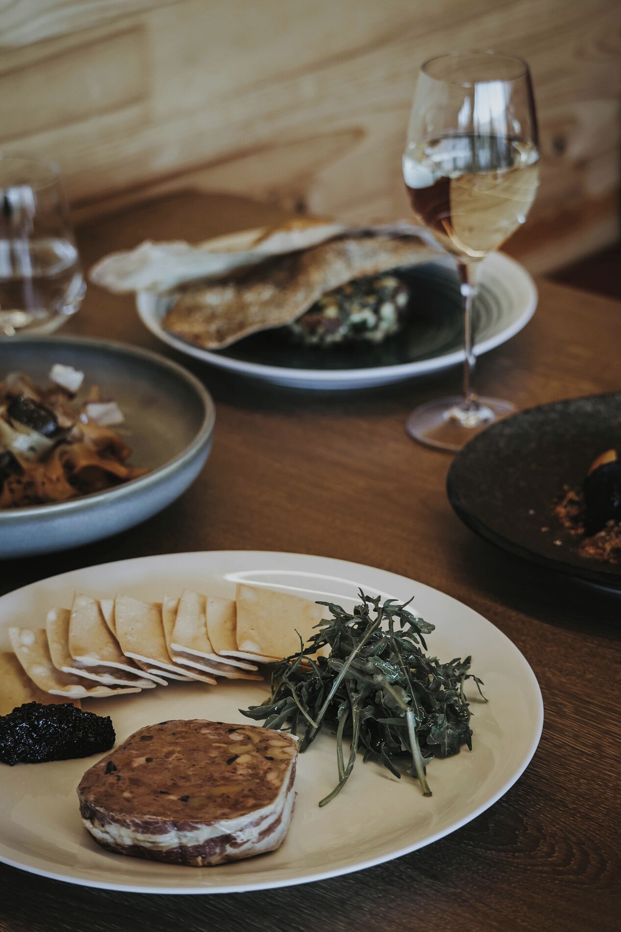 Une table à manger avec différents plats, notamment une assiette de viande tranchée, un saladier de légumes verts et un verre de vin.