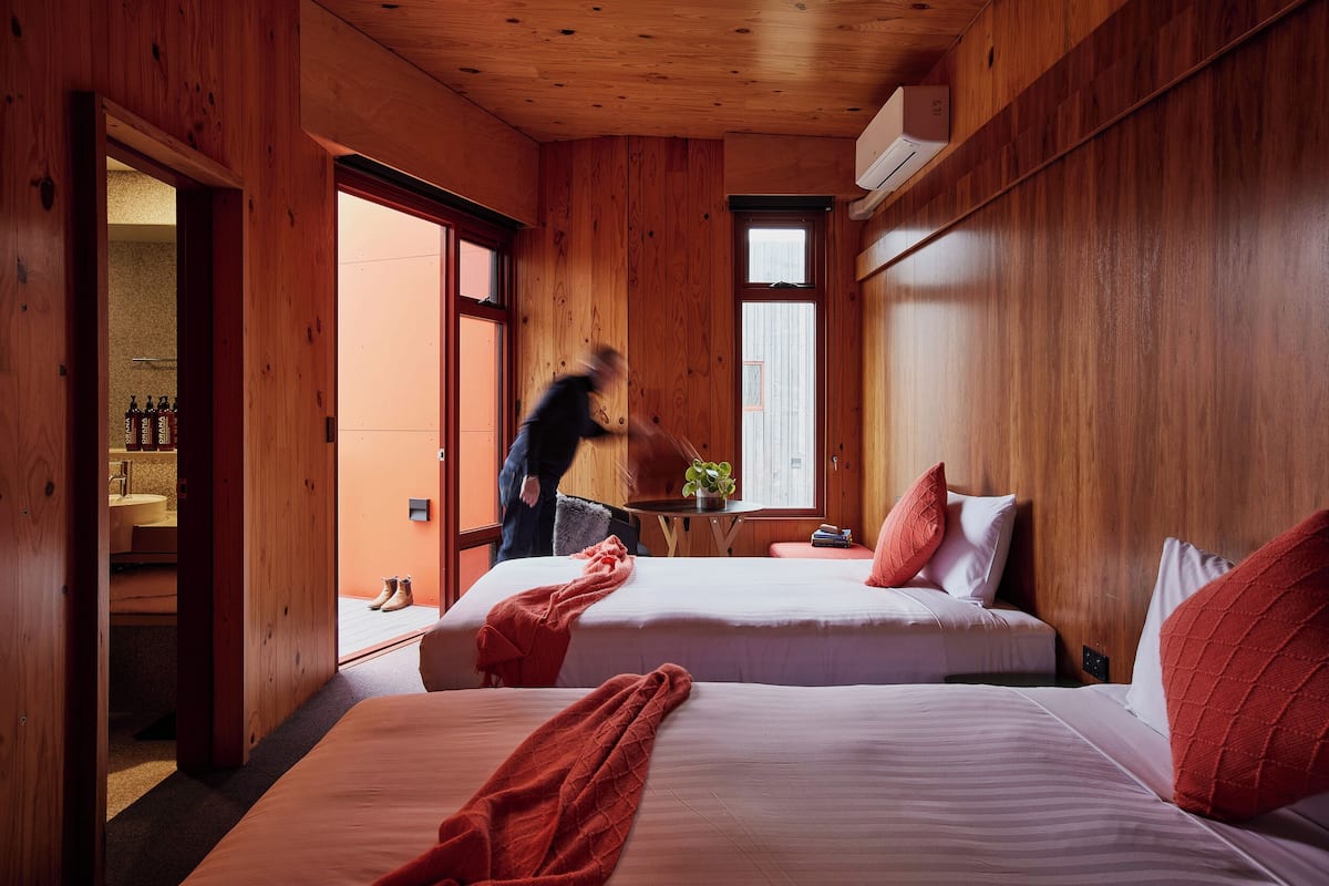 A wooden room with two beds, a small table with a plant, and a window.