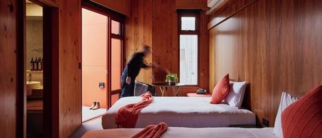Una habitación de madera con dos camas, una mesita con una planta y una ventana.
