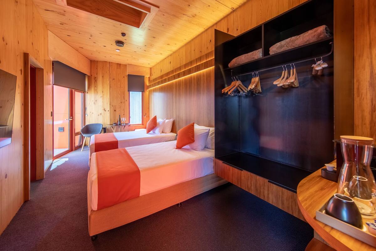 A hotel room with wooden walls, two beds, a TV, a desk, and a seating area.