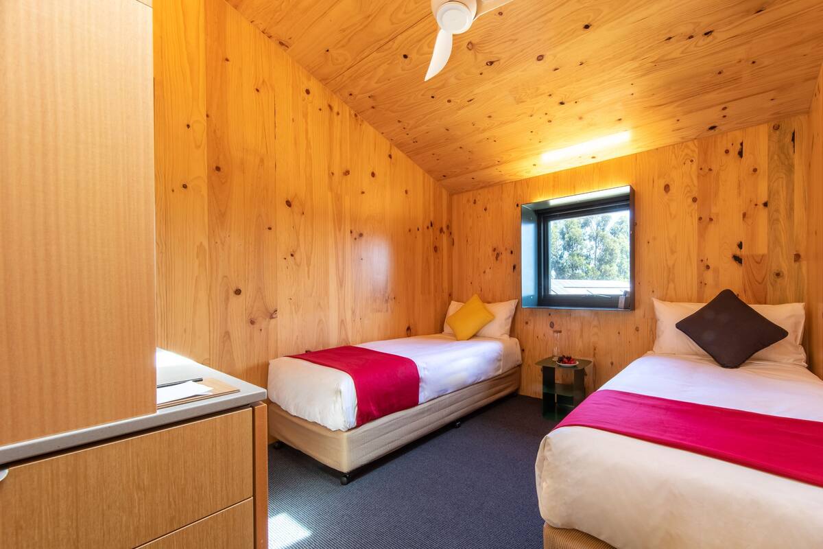 A wooden cabin room with two beds, a window, and a ceiling fan.