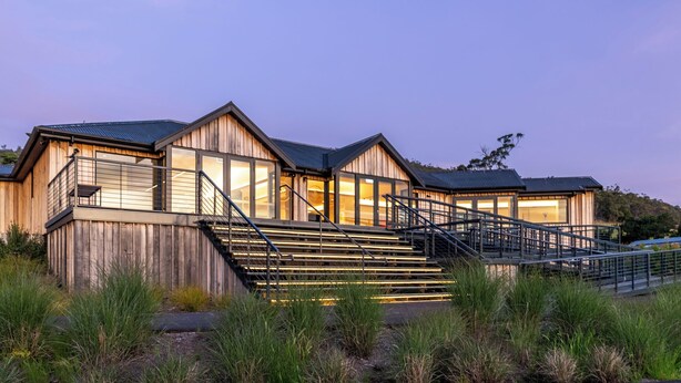 A wooden cabin with a staircase leading to a deck, surrounded by grass.