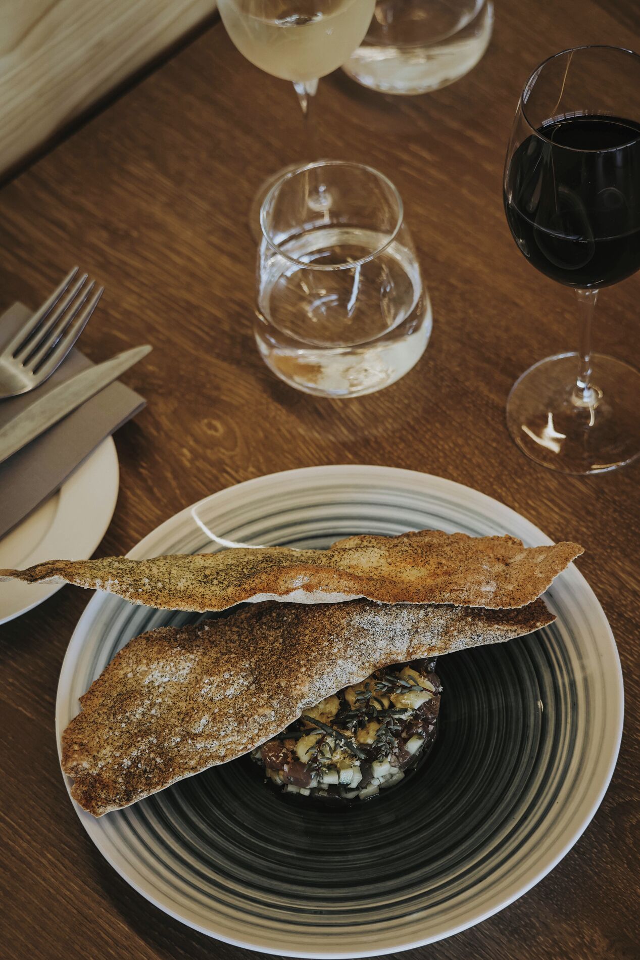A plate with a fish fillet and a side dish, accompanied by a fork and knife on a wooden table.