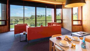 A modern room with large windows, a sofa, a dining table with breakfast, and a view of the countryside.