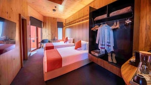 A wooden interior with two beds, a seating area, and a clothing rack.