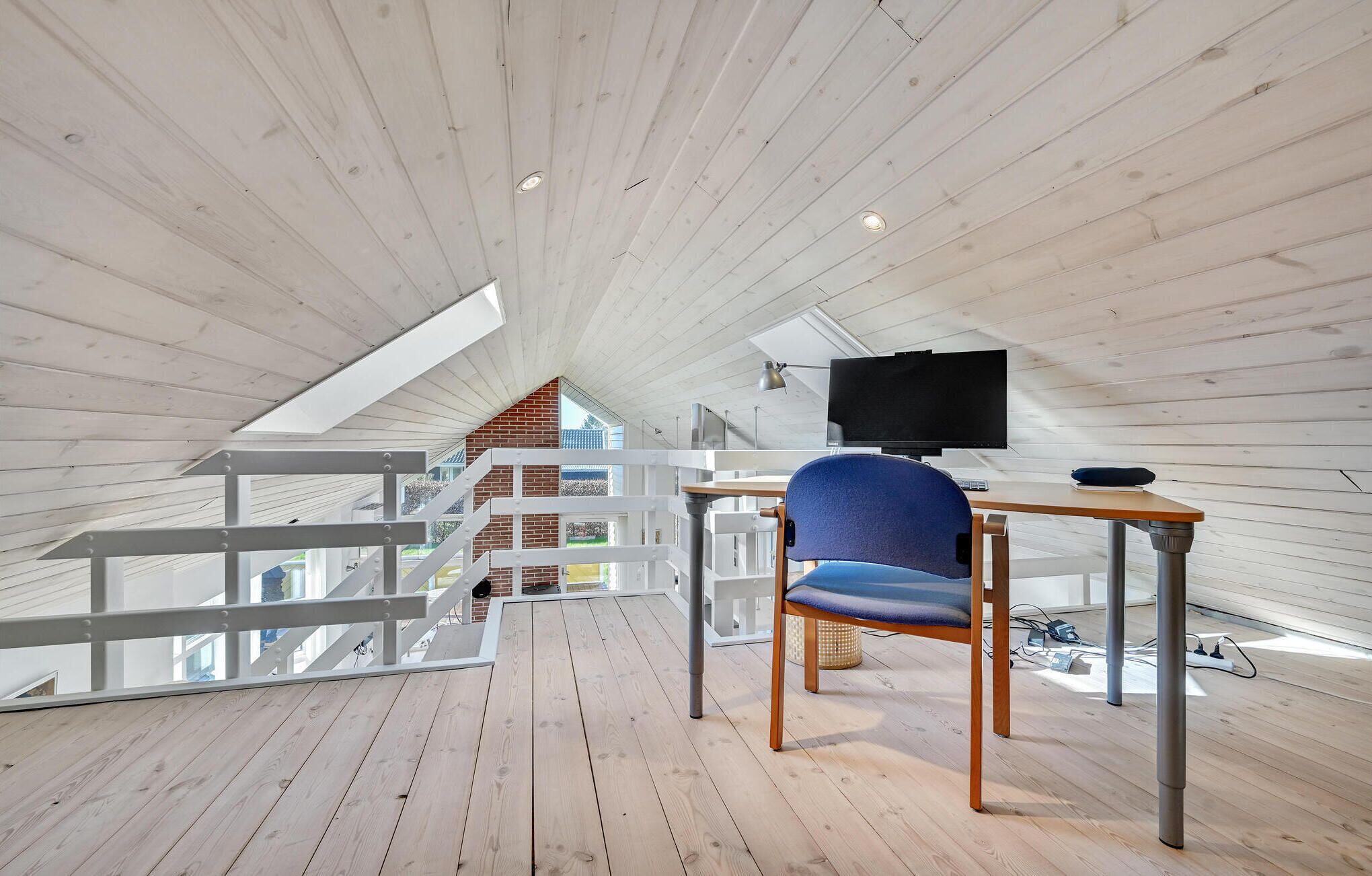 Un intérieur moderne avec un plafond en bois, un bureau avec une chaise, un téléviseur et une vue sur l’extérieur.