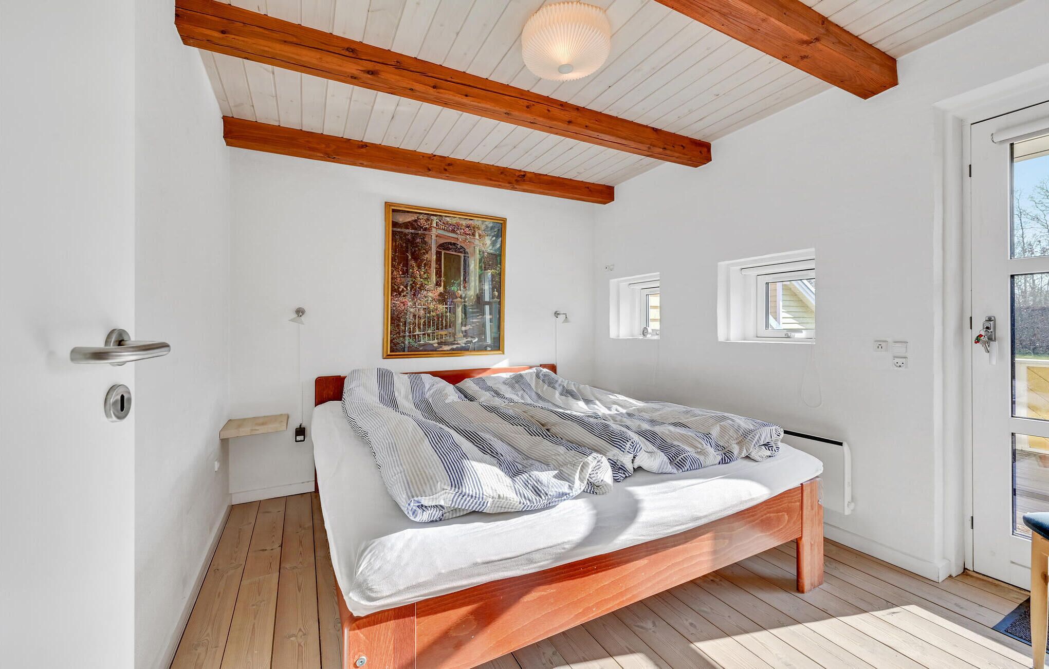 Une chambre à coucher avec un lit en bois, un tableau au mur et une fenêtre donnant sur un beau paysage.
