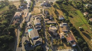 Vue aérienne d’un quartier résidentiel situé sur la côte, avec des maisons, une piscine et une plage en arrière-plan.