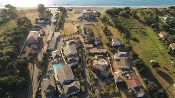 Vista aérea de una zona residencial costera con casas, piscina y una playa al fondo.