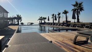 Un espace aménagé au bord de la piscine, avec des chaises longues et des parasols, une terrasse en bois et une vue sur la mer.