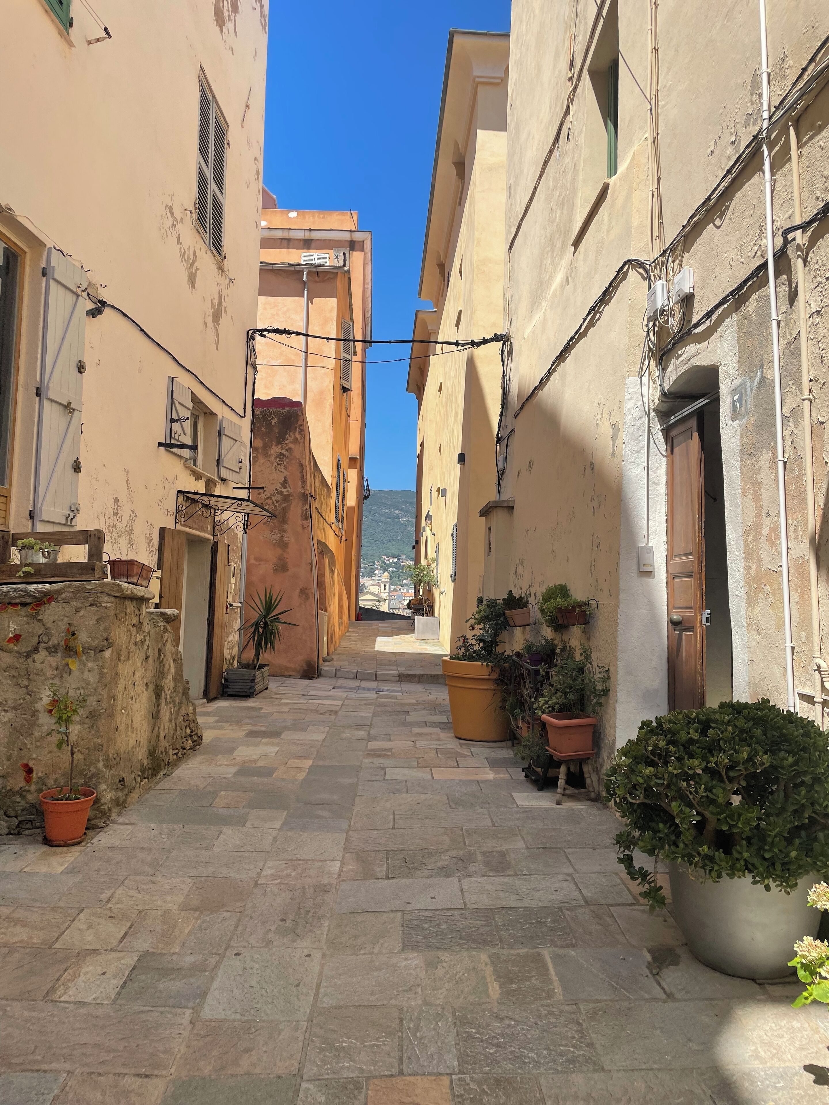 Un stretto vicolo fiancheggiato da edifici, con piante in vaso e un cielo azzurro intenso.