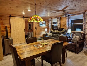 Un accogliente interno di una baita con un tavolo da pranzo in legno, un divano in pelle e una ventola a soffitto.