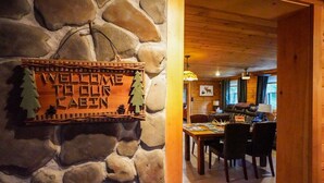A stone wall with a welcome sign and a dining area with a table and chairs. - Pinecone Place - A True North Vacation Home (Long Lake)