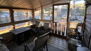 A covered outdoor seating area with tables and chairs, a ceiling fan, and a view of the surrounding landscape. - Pinecone Place - A True North Vacation Home (Long Lake)