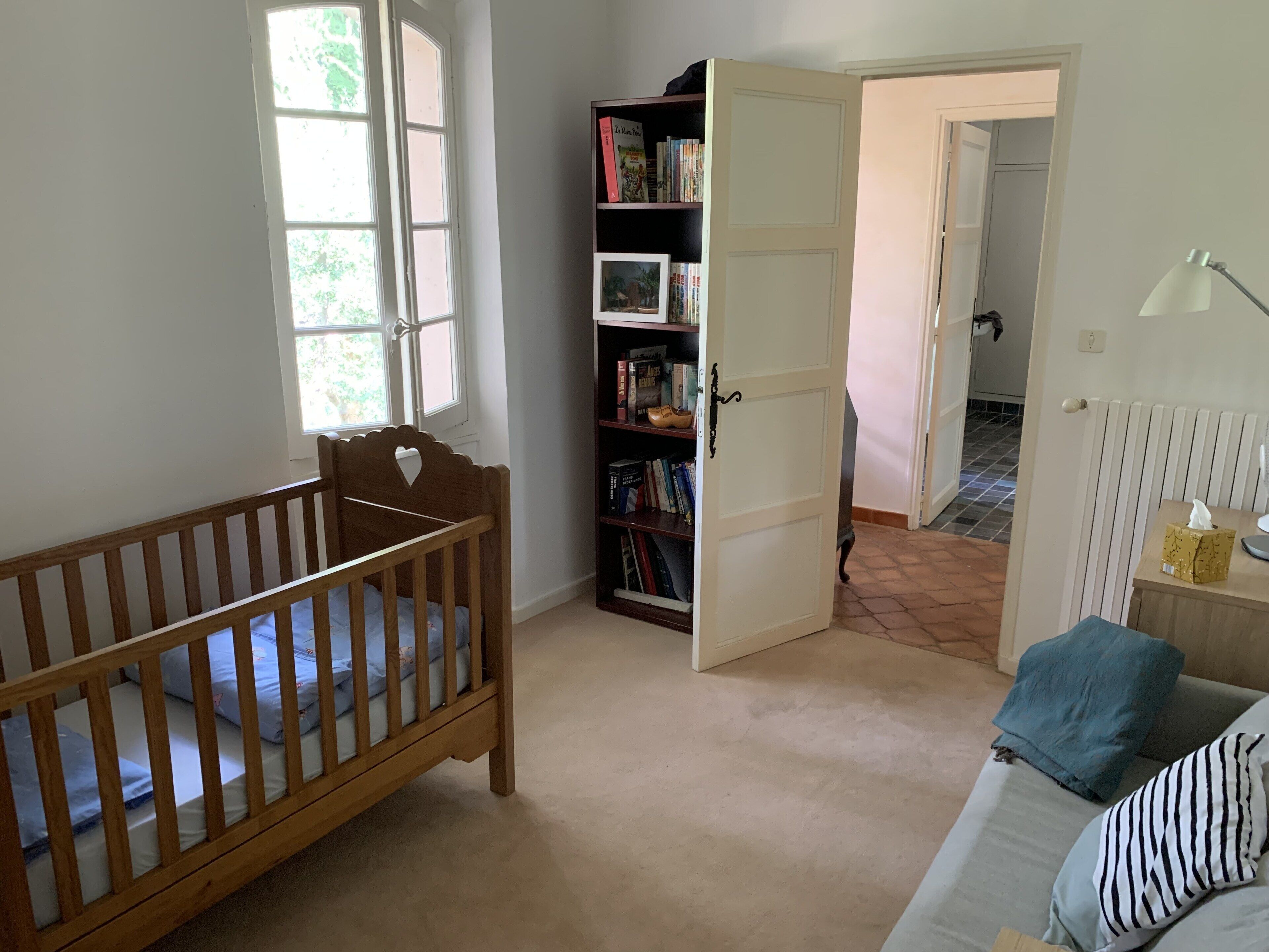 Una habitación con una cuna de madera, una estantería y una puerta que da a otra habitación.