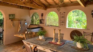 Zona d'exterior per dinar amb taula de fusta rústica, plantes en testos i una barbacoa.