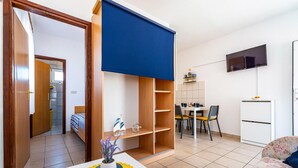 Een knus woongedeelte met een eethoek, een aan de muur bevestigde televisie en een kleine kitchenette.