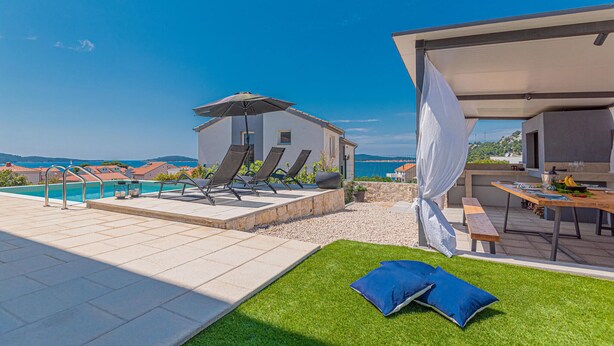 Un área de piscina en la azotea con sillones de descanso, un espacio de estar cubierto y vista al mar.