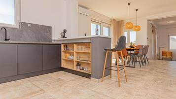 A modern kitchen with grey cabinets, a marble countertop, and a built-in wine rack. There is a dining area with a table and chairs, and a large window providing natural light.