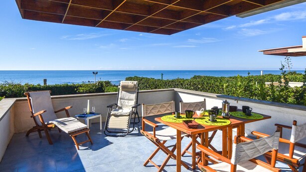 A terrace with a wooden table and chairs, a view of the ocean, and a clear sky. - Nice apartment in Castglione Della P. (Castglione Della P.)