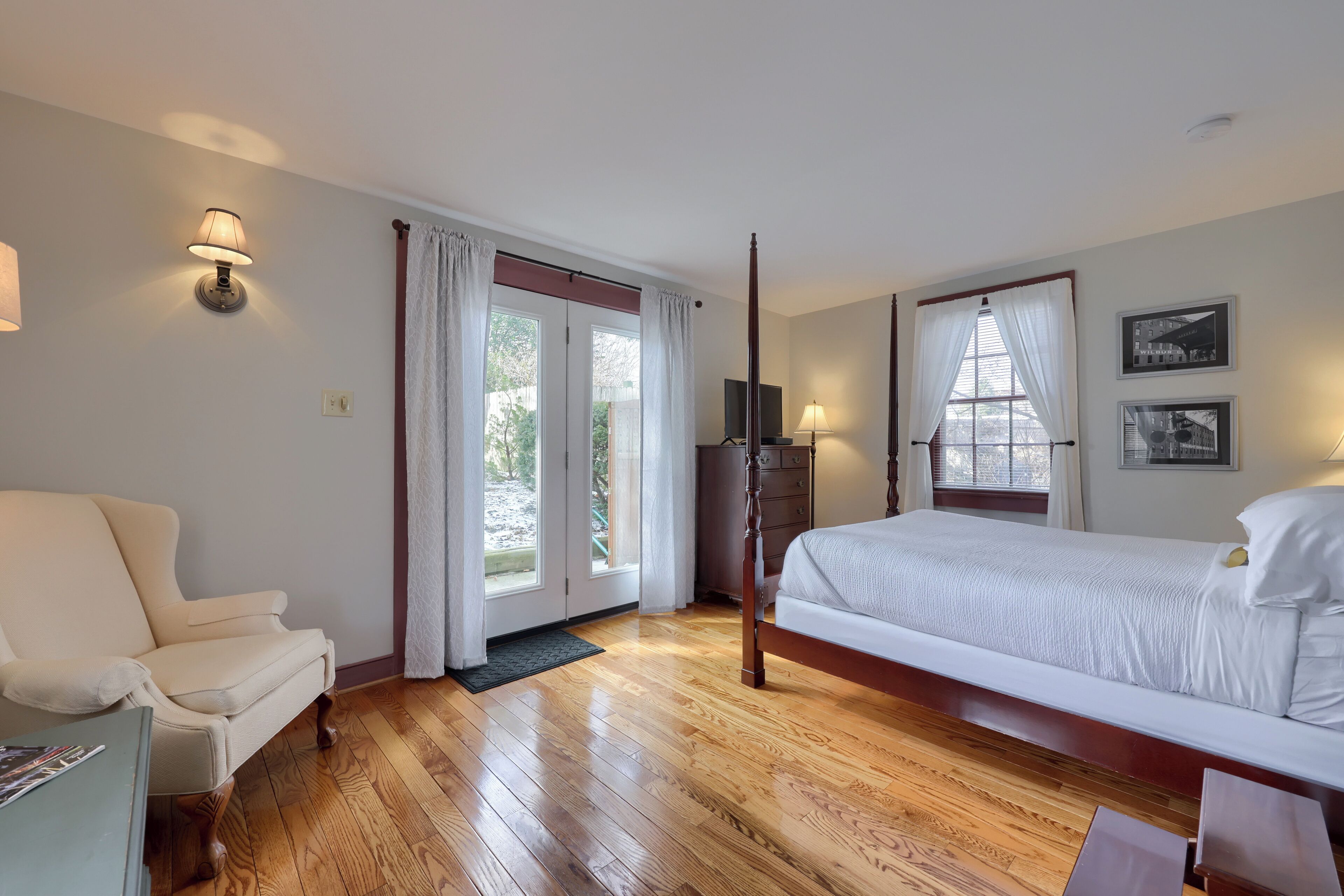 Un dormitorio con piso de madera, una cama, una silla, un escritorio y un televisor.