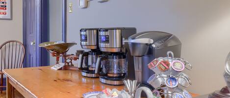A coffee station with multiple coffee makers and a mug rack.