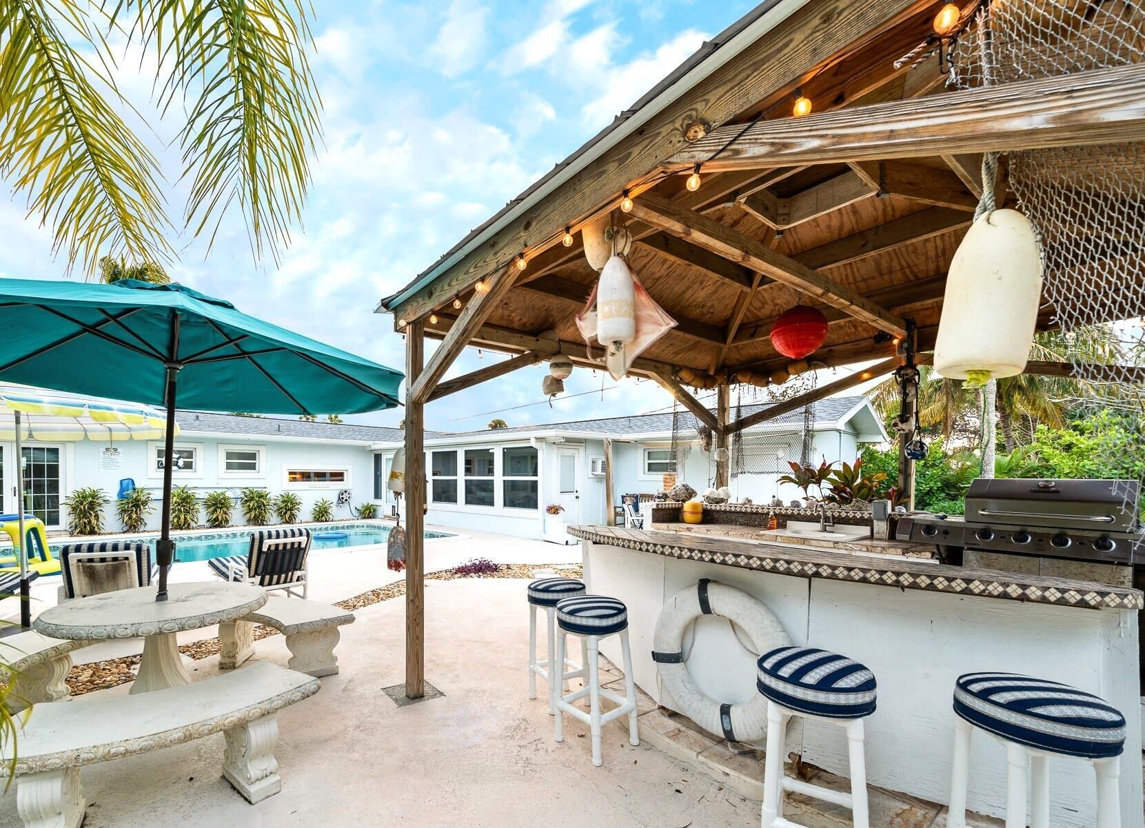 Un espace bar extérieur avec une piscine, des tabourets de bar et un bar de style tiki.