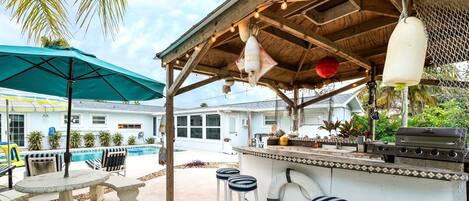 Un espace bar extérieur avec une piscine, des tabourets de bar et un bar de style tiki.